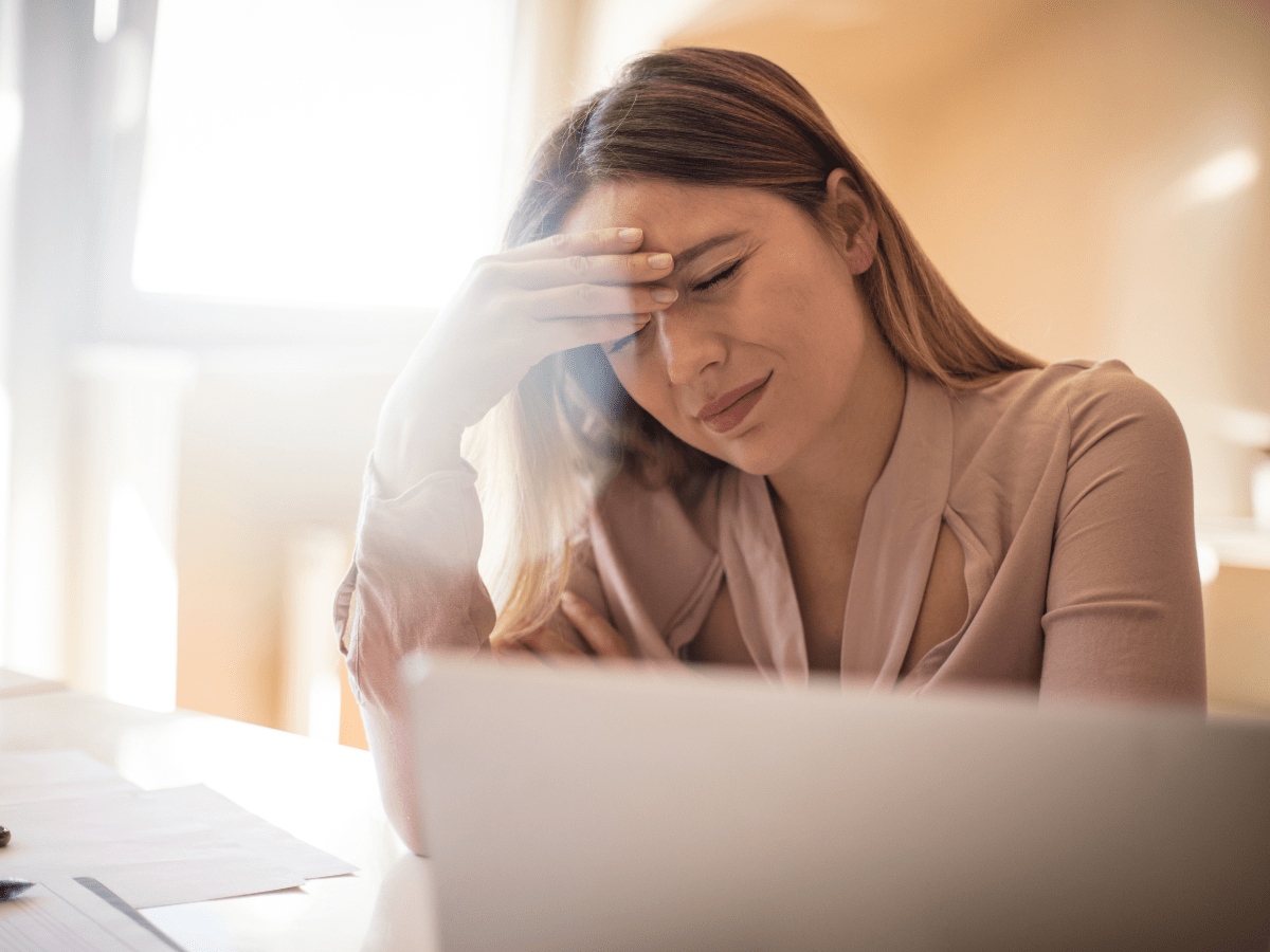 a woman sitting in front of a laptop with her hand on her head, in pain