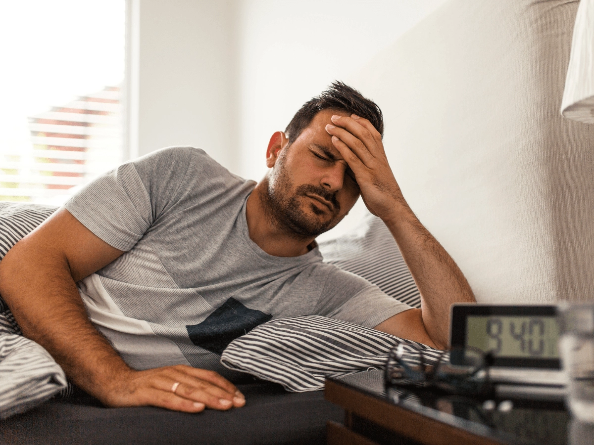 mens-migraine a man lying in bed with his hand on his head in pain