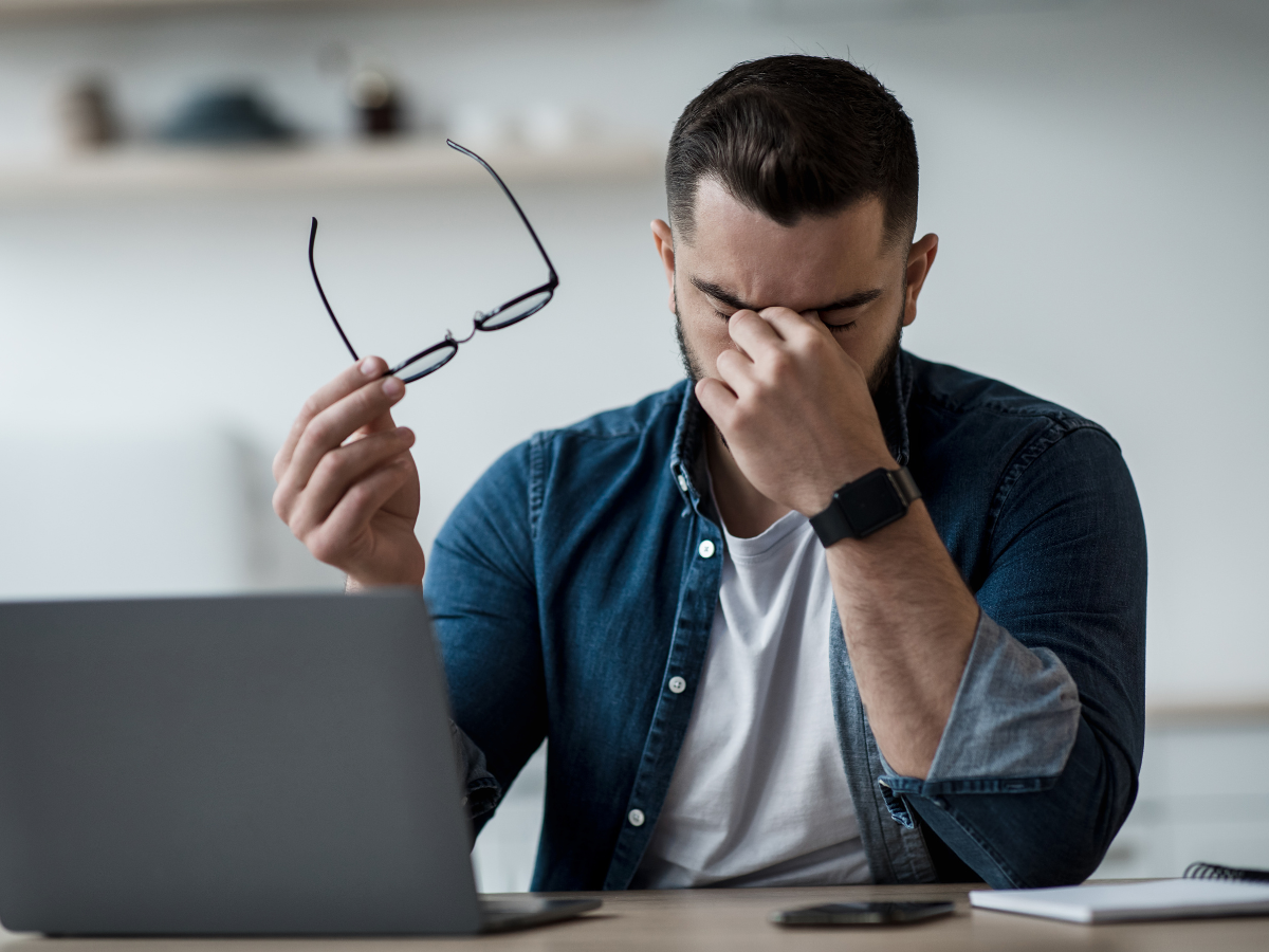 a man sitting at a desk with his hand rubbing his eye, with a tension headache