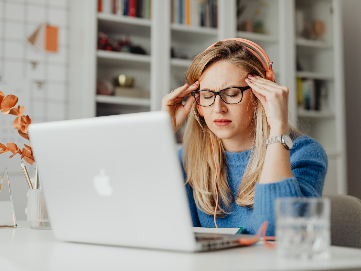 a woman sitting at a desk holding her head in pain with a headache