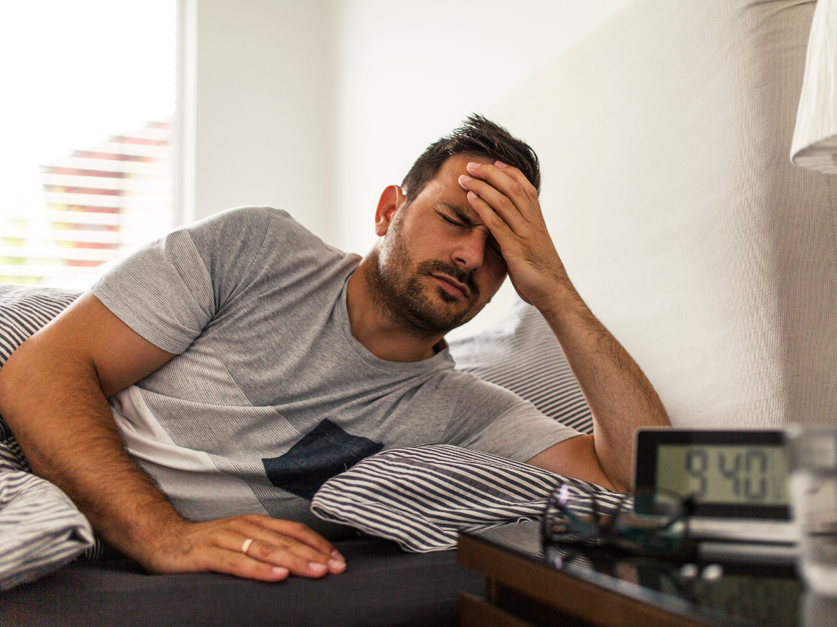 a man lying in bed with his hand on his head in pain